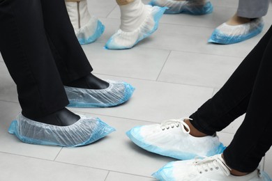 Women wearing blue shoe covers onto different footwear indoors, closeup