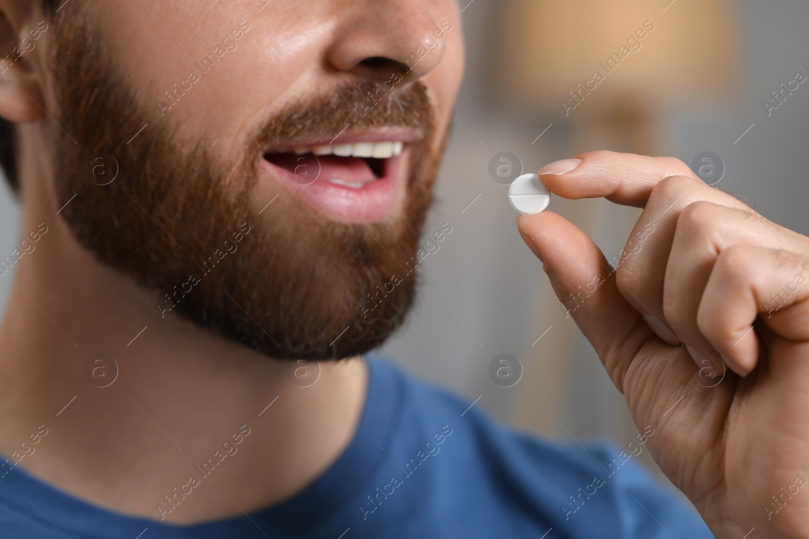 Photo of Closeup view of bearded man taking pill on blurred background