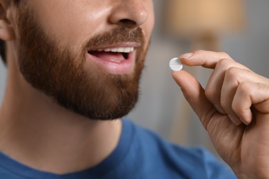 Photo of Closeup view of bearded man taking pill on blurred background