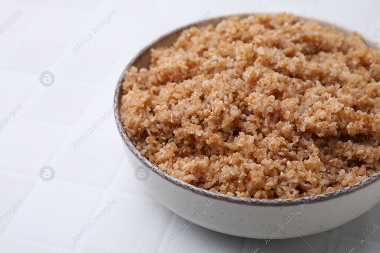 Photo of Tasty wheat porridge in bowl on white tiled table, closeup. Space for text