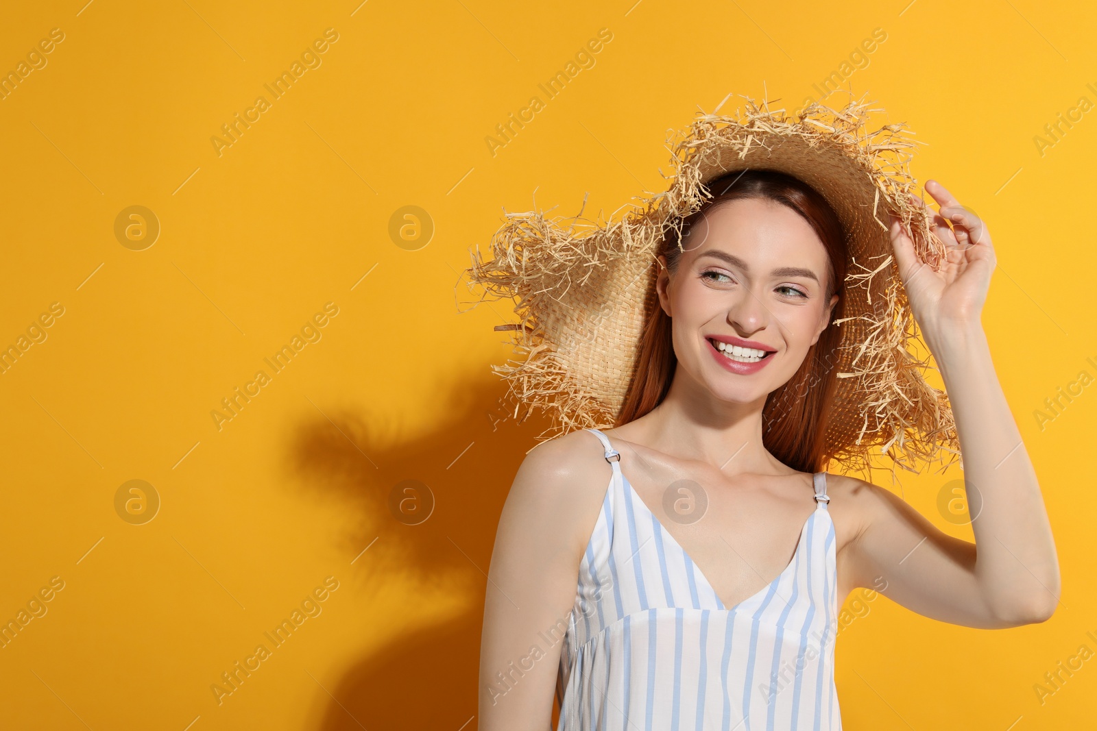 Photo of Beautiful young woman in straw hat on orange background, space for text