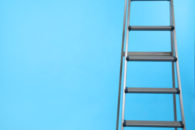 Photo of Metal stepladder on light blue background. Space for text