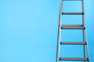 Metal stepladder on light blue background. Space for text