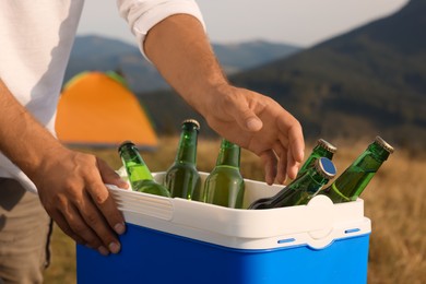 Man taking bottle of beer from cool box in nature, closeup