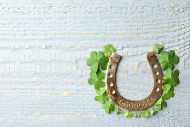 Photo of Clover leaves and horseshoe on wooden table, flat lay with space for text. St. Patrick's Day celebration