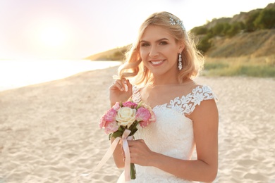 Photo of Happy bride holding wedding bouquet on beach