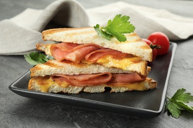 Photo of Tasty sandwiches with ham, parsley and melted cheese on grey textured table, closeup