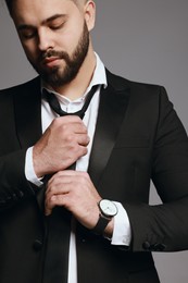 Handsome bearded man tightening tie on grey background