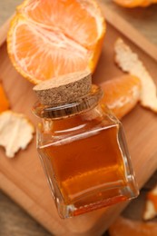 Photo of Bottle of tangerine essential oil and peeled fresh fruit on wooden table, flat lay