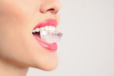 Photo of Young woman holding ice cube in mouth on light background, closeup. Space for text