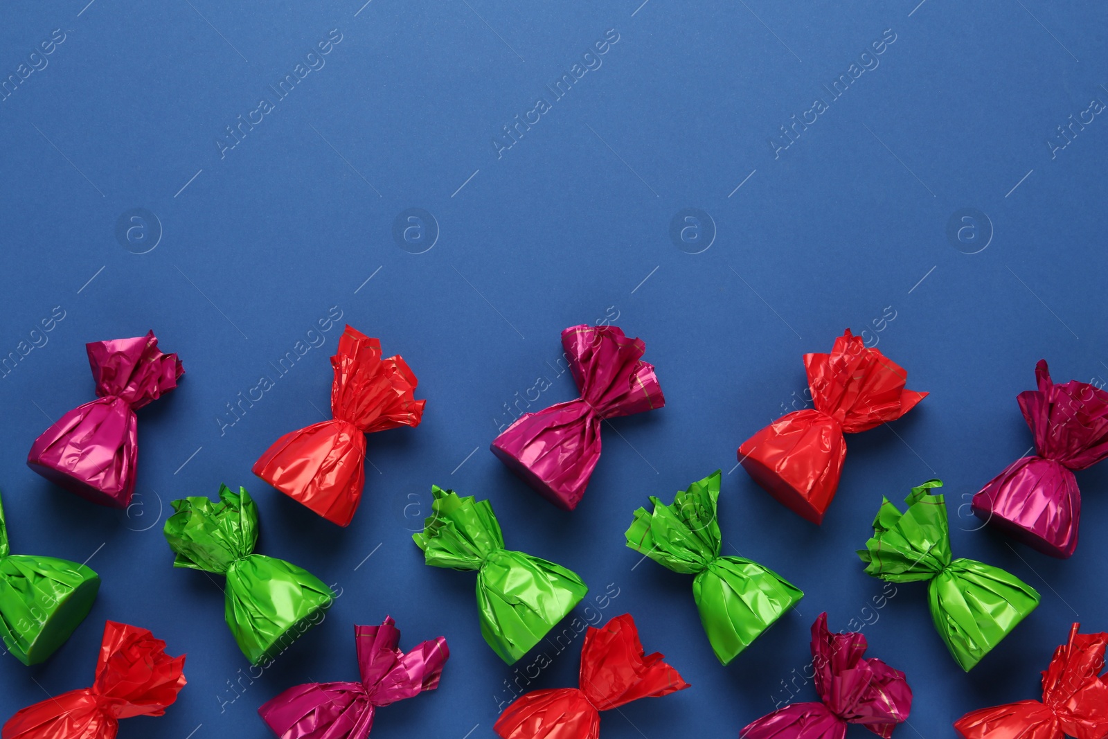 Photo of Many candies in colorful wrappers on blue background, flat lay. Space for text