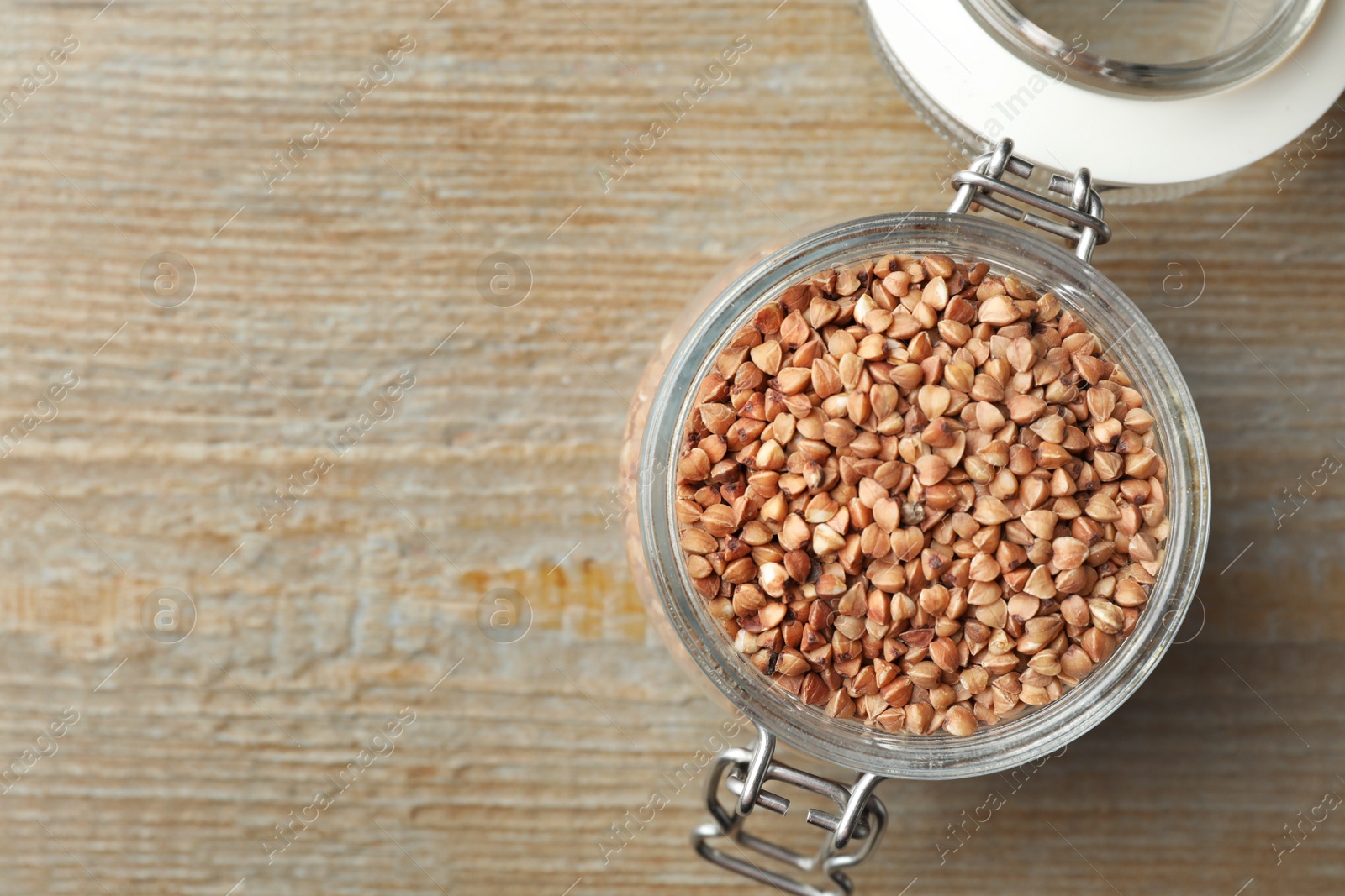 Photo of Buckwheat grains in jar on wooden table, top view. Space for text