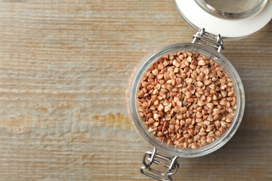 Photo of Buckwheat grains in jar on wooden table, top view. Space for text