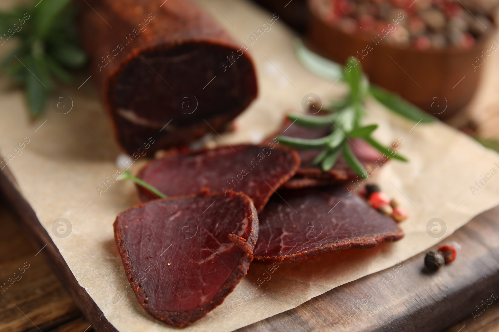 Photo of Delicious dry-cured beef basturma with rosemary and peppercorns on wooden table, closeup