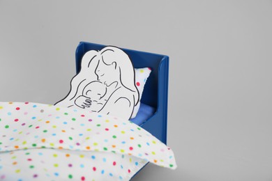 Photo of Maternity leave concept. Paper cutout of mother and child on toy bed against light grey background, space for text