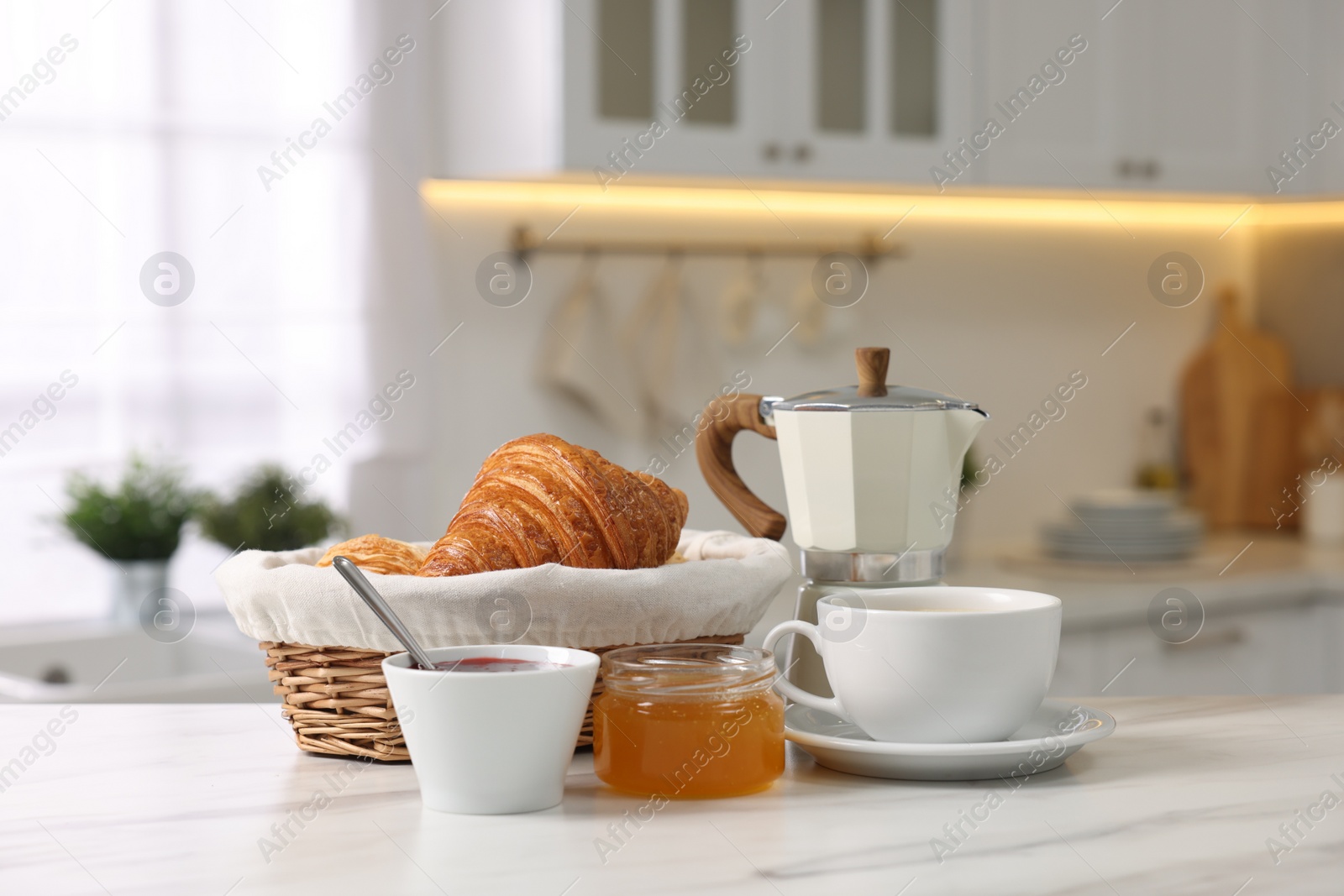 Photo of Breakfast served in kitchen. Fresh croissants, jam, honey and coffee on white table