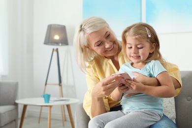 Photo of Little girl with her grandmother using smartphone at home, space for text. Family time