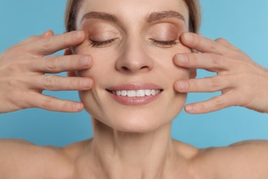 Photo of Woman massaging her face on turquoise background