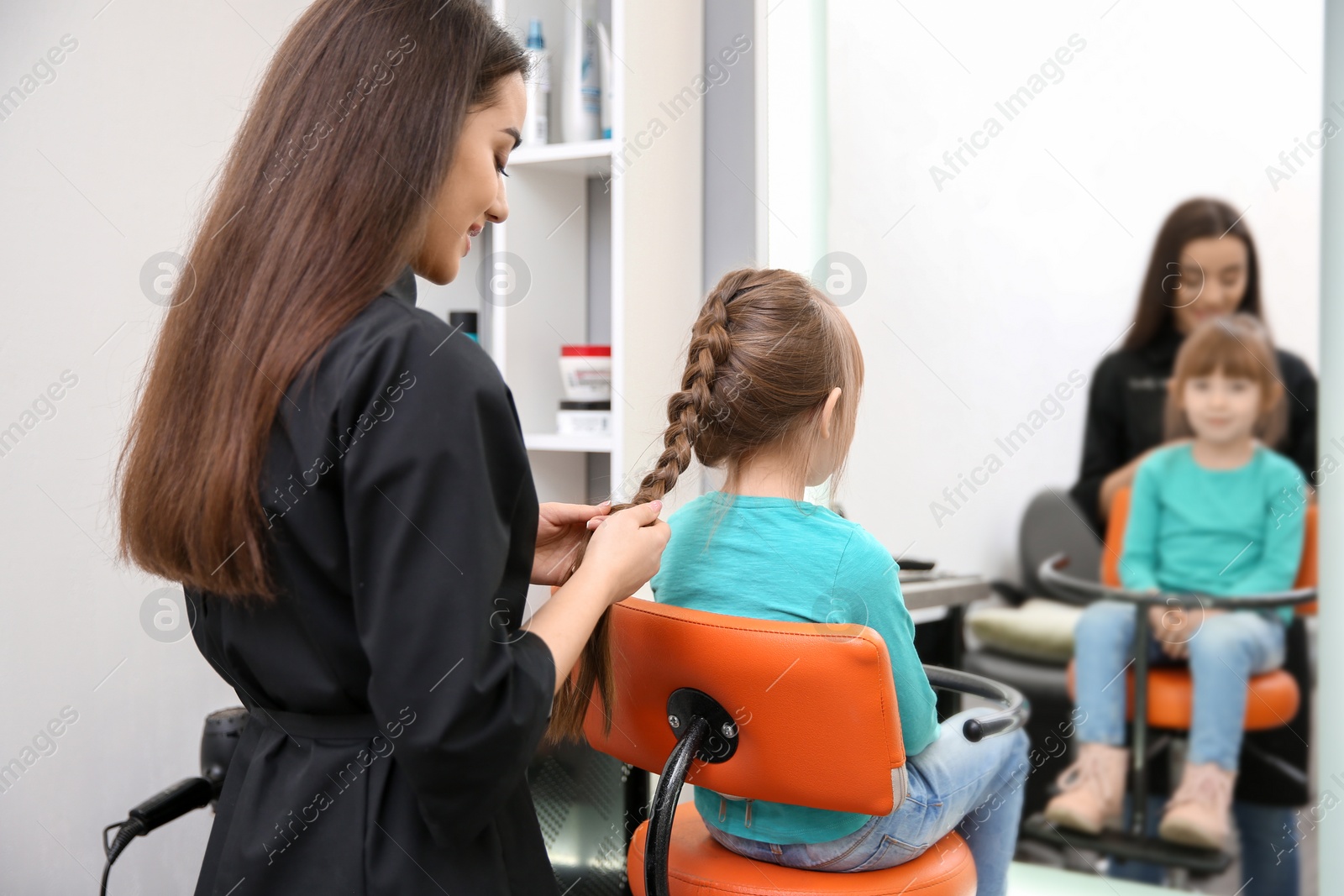 Photo of Professional female hairdresser working with little girl in salon