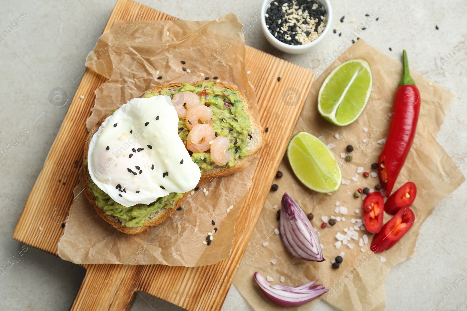 Photo of Delicious sandwich with guacamole, shrimps, fried egg and ingredients on light grey table, flat lay