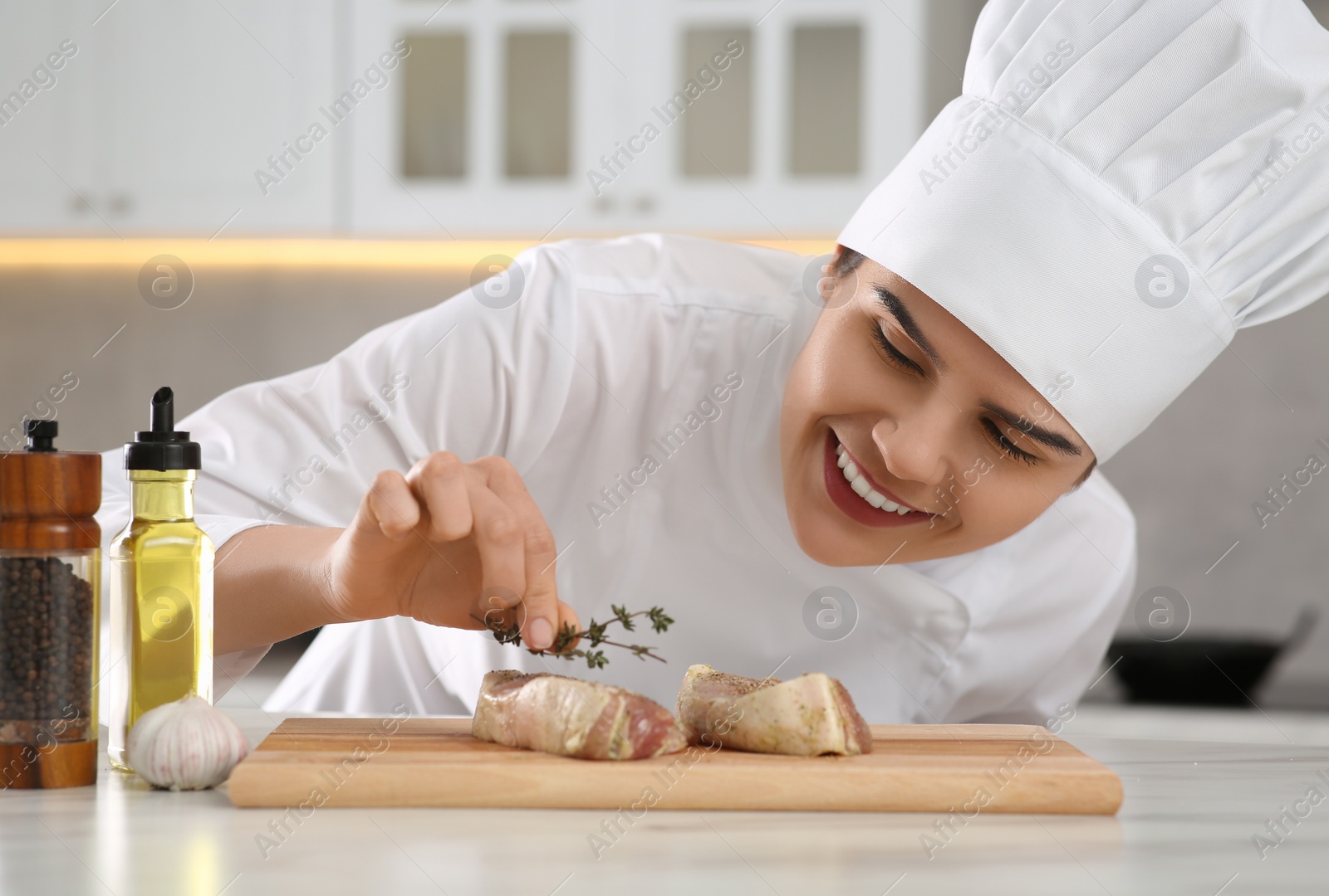 Photo of Professional chef decorating delicious meat with thyme at white marble table