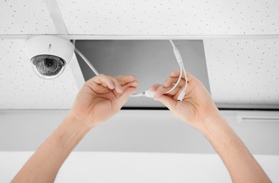 Technician installing CCTV camera on ceiling indoors, closeup