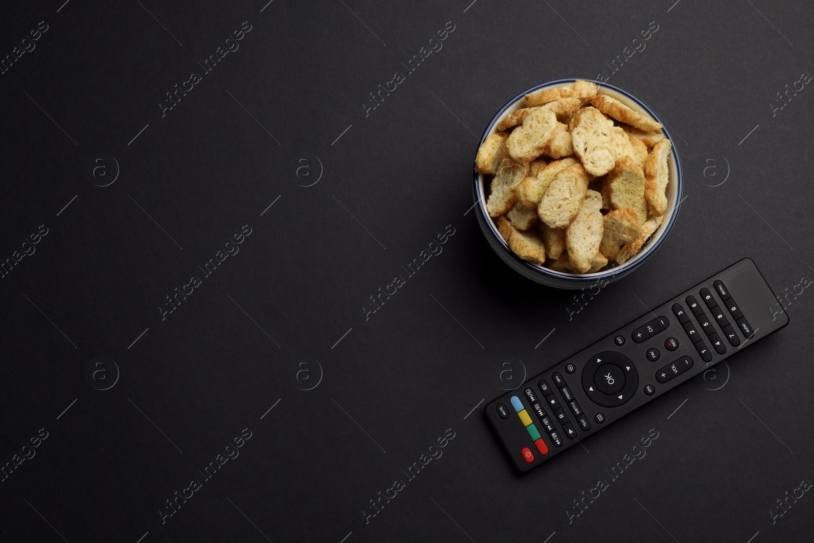 Photo of Modern tv remote control and rusks on black background, flat lay. Space for text
