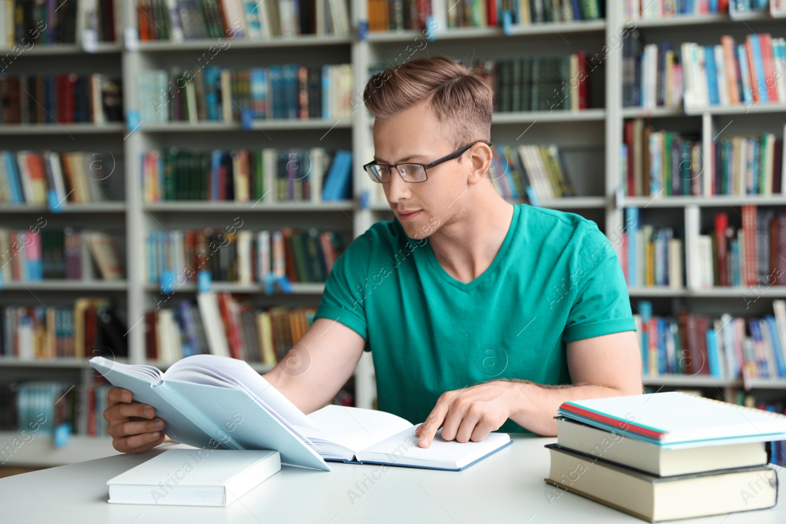 Photo of Young man reading book at table in library