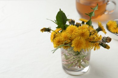 Photo of Beautiful dandelion bouquet near delicious fresh tea on white table. Space for text