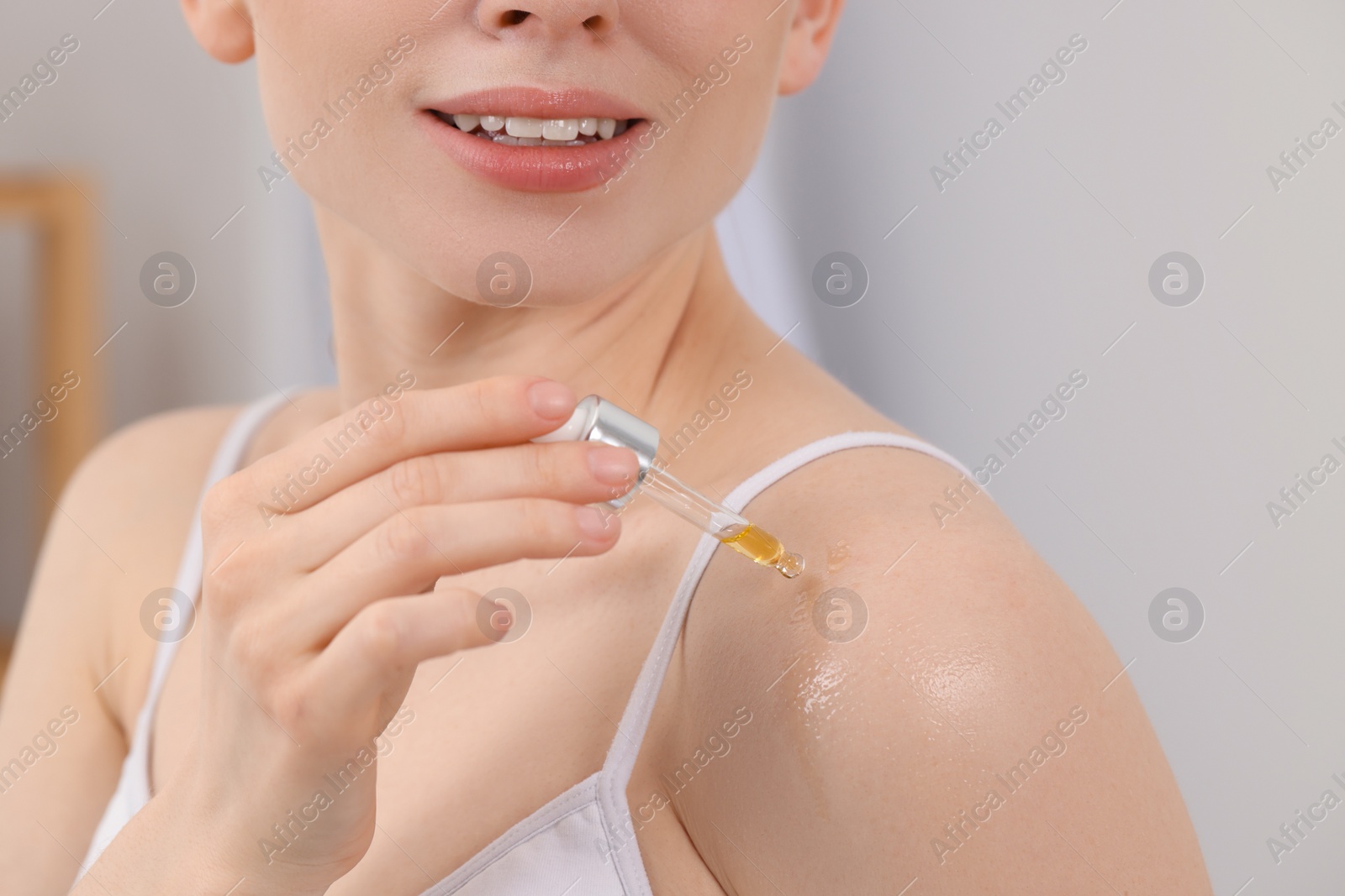 Photo of Woman applying essential oil onto shoulder on blurred background, closeup