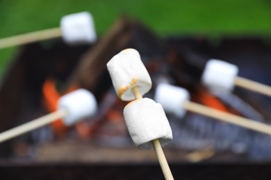 Photo of Delicious puffy marshmallows roasting over bonfire, closeup