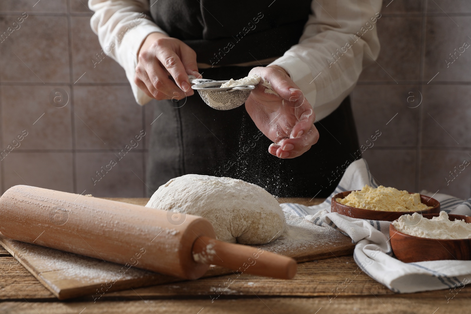 Photo of Woman sprinkling flour over dough at wooden table, closeup
