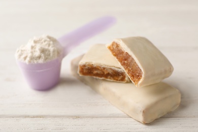 Photo of Tasty protein bars and scoop of powder on white table