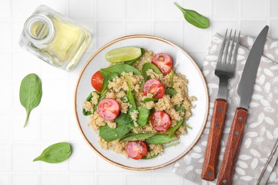 Delicious quinoa salad with tomatoes and spinach leaves served on white tiled table, flat lay
