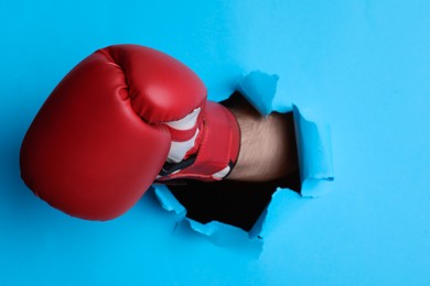 Photo of Man breaking through light blue paper with boxing glove, closeup