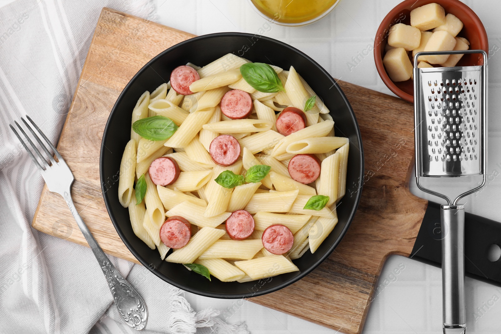 Photo of Tasty pasta with smoked sausage and basil served on white tiled table, flat lay