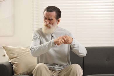 Senior man suffering from pain in hand on sofa at home. Rheumatism symptom