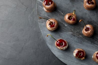 Photo of Sweet chocolate dipped cherries on black table, top view. Space for text