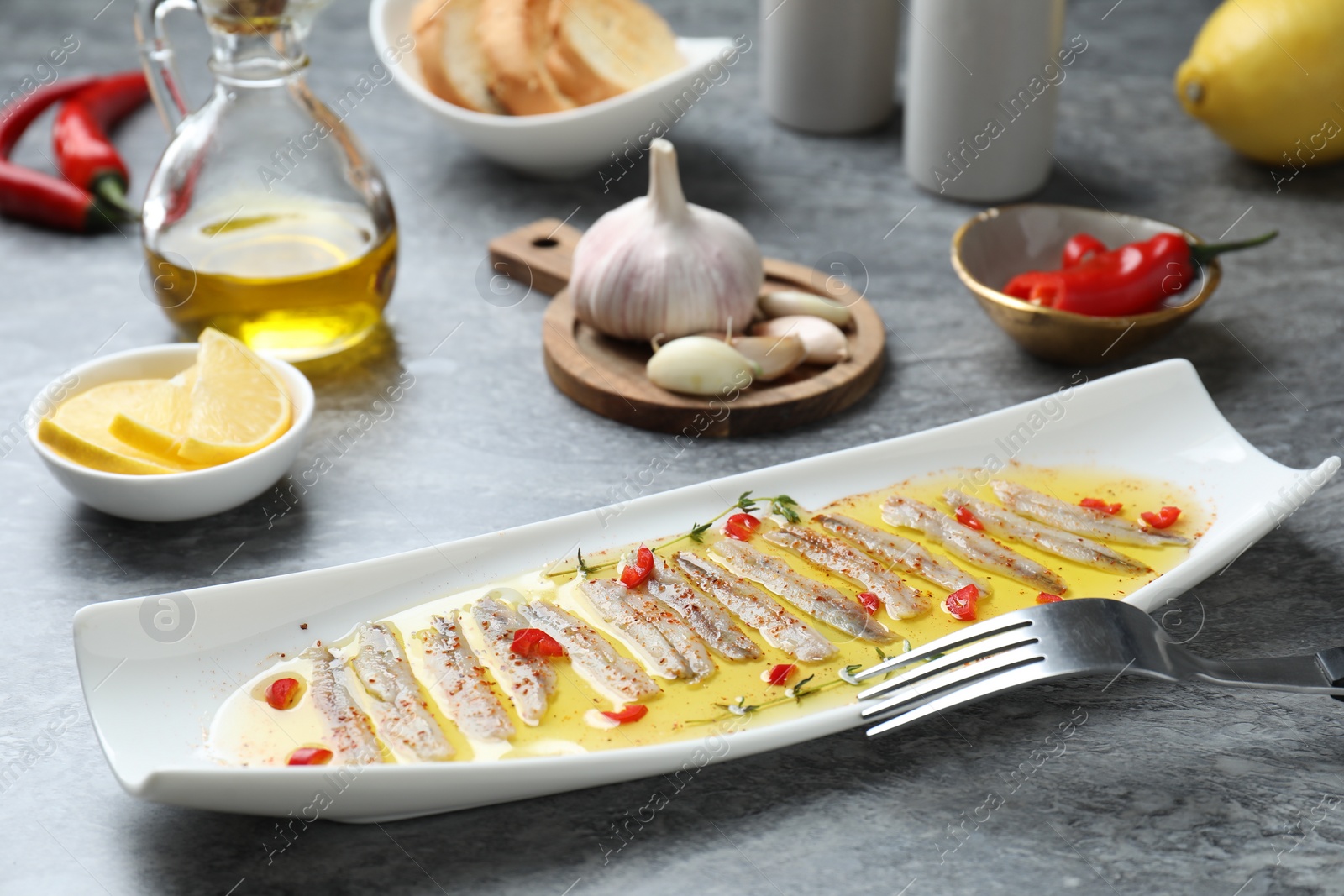 Photo of Tasty pickled anchovies with spices and products on gray table