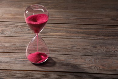 Hourglass with pink flowing sand on wooden table. Space for text