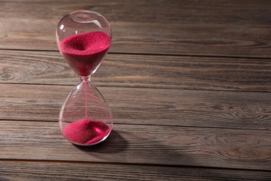 Photo of Hourglass with pink flowing sand on wooden table. Space for text