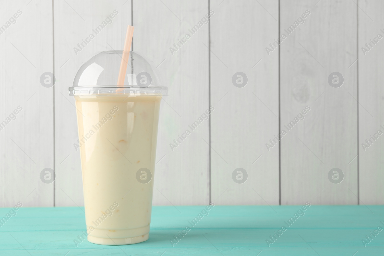 Photo of Tasty smoothie in plastic cup on light blue table against white wooden wall. Space for text