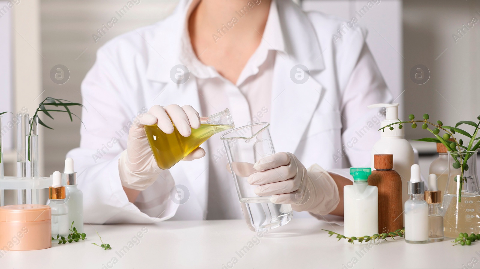 Photo of Dermatologist developing cosmetic product at white table indoors, closeup