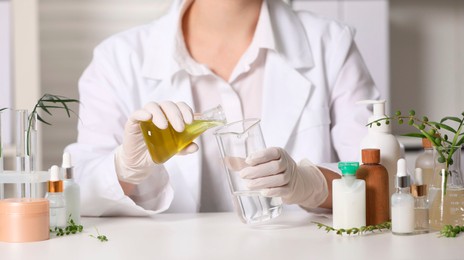 Photo of Dermatologist developing cosmetic product at white table indoors, closeup