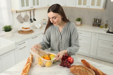 Woman with string bag of fresh fruits, baguettes and bread on light marble table, above view