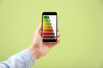 Energy efficiency rating on smartphone display. Man holding device on light green background, closeup