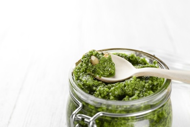 Photo of Jar of pesto sauce with spoon on table, closeup. Space for text