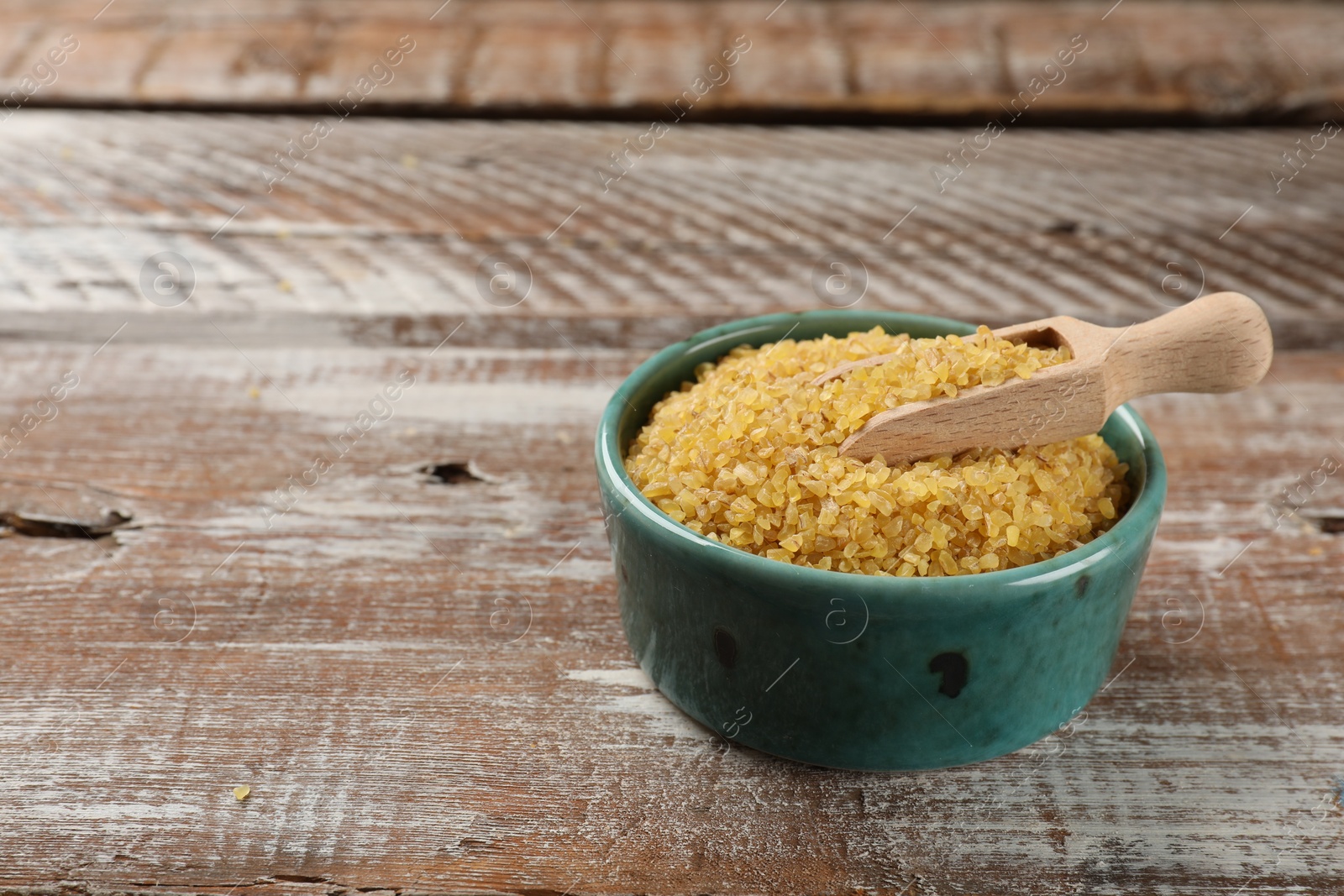 Photo of Bowl and scoop with raw bulgur on wooden table, space for text