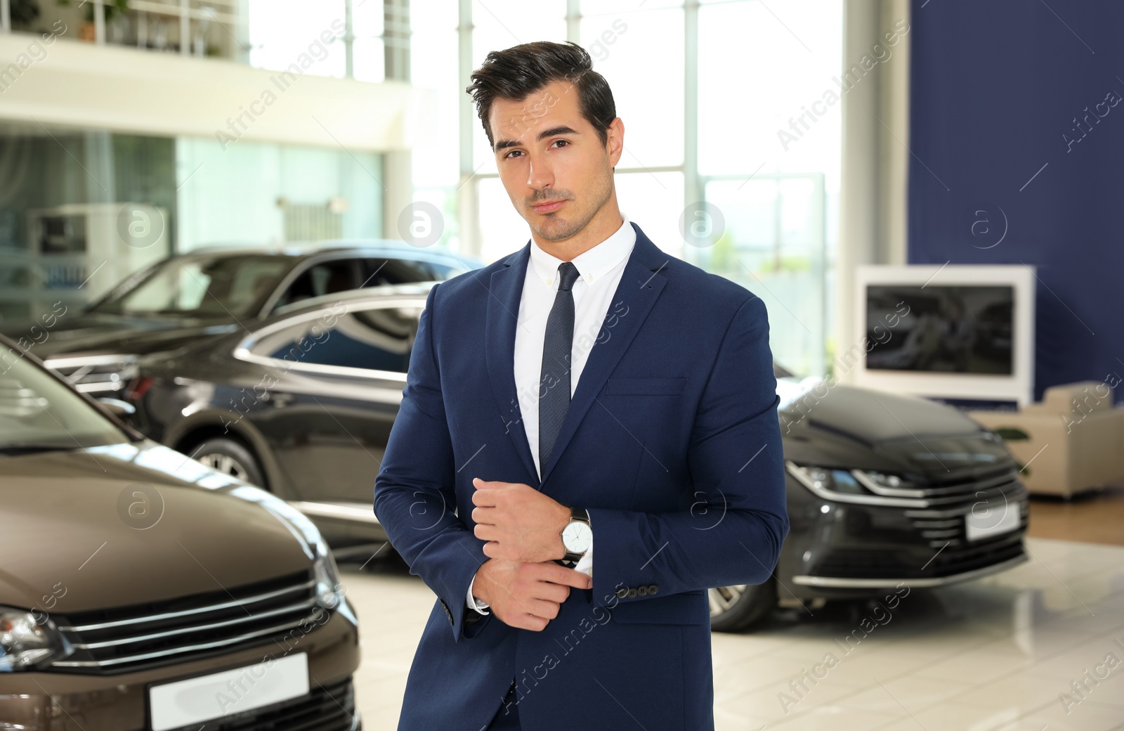 Photo of Young salesman near new car in modern dealership