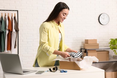 Photo of Seller packing clothes into cardboard box at table in office. Online store